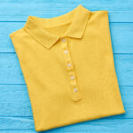 Beautiful yellow polo t-shirt isolated. New trendy item for summer resort, blue background.